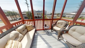 A covered outdoor seating area with wicker furniture and cushions, a small table, and a view of residential buildings in the background. - Cherry Grove 2 bedroom condo, just a block off the beach.  (North Myrtle Beach)