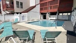 A swimming pool with lounge chairs and a building with a red facade. - Cherry Grove 2 bedroom condo, just a block off the beach.  (North Myrtle Beach)