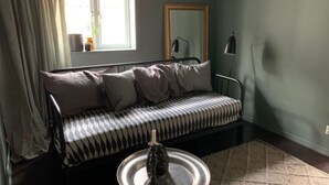 A room with a black and white striped sofa, a small round table with a decorative item, a window with curtains, and a mirror on the wall. - Charmant 1 RoK Visby Innerstad, last round (Gotlands län)