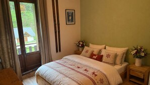 Een slaapkamer met een bed, een houten nachtkastje, een raam met gordijnen en een deur.