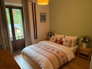 Een slaapkamer met een bed, een houten nachtkastje, een raam met gordijnen en een deur.