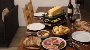Een eettafel gedekt met verschillende soorten eten, een kaasrasper, borden, bestek en een fles wijn.