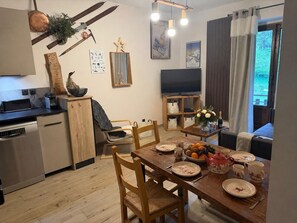 A dining area with a wooden table set for four, a television, and a kitchen area with a dishwasher and cabinets.