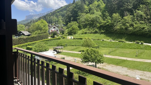Uitzicht vanaf een balkon over een groen landschap, met een huis en een berg op de achtergrond.