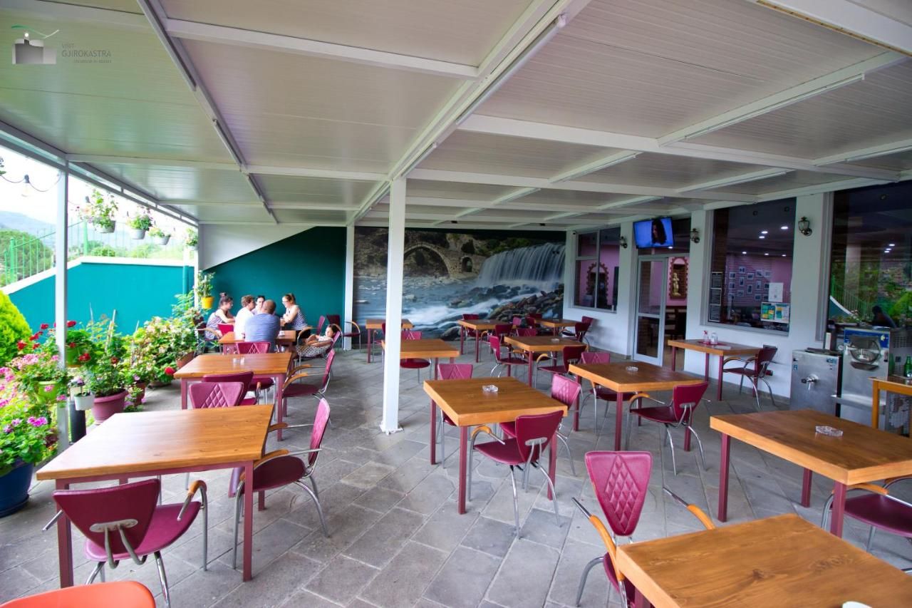 An outdoor café with tables and chairs, a mural of a waterfall, and a view of a bridge.