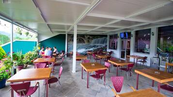 An outdoor café with tables and chairs, a mural of a waterfall, and a view of a bridge.