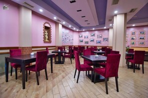 A restaurant with multiple tables and chairs, a brick wall with pictures, and a statue. - Hotel Alvero (Përmet)