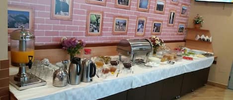 Montaje de bufé con diversos alimentos y bebidas, pared de ladrillo con cuadros enmarcados y un televisor montado.