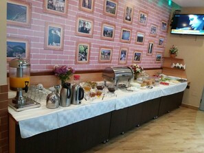 Montaje de bufé con diversos alimentos y bebidas, pared de ladrillo con cuadros enmarcados y un televisor montado.