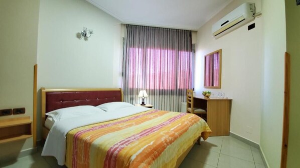 A bedroom with a bed, a nightstand, a lamp, a mirror, and a window with curtains.