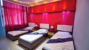 Habitación de hotel con tres camas dispuestas en fila, una pared de acento roja y una ventana con cortinas rojas.