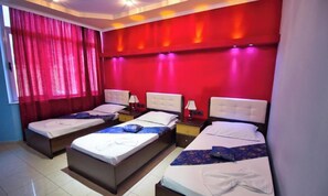 A hotel room with three beds, red walls, and a window with curtains. - Hotel Alvero (Përmet)