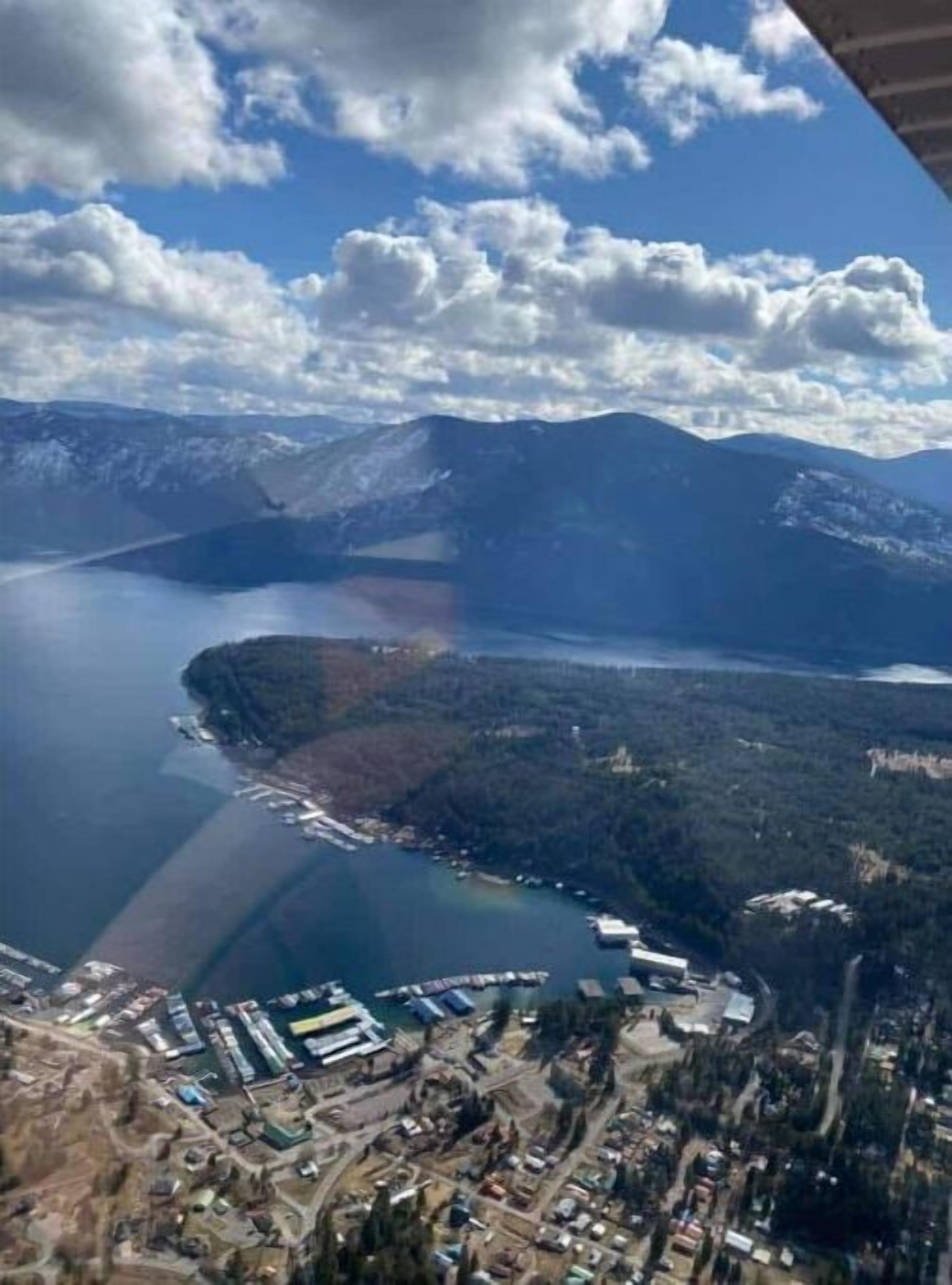 Luchtbeeld van een kustgebied met bergen op de achtergrond, een groot wateroppervlak en een bebouwd gebied met gebouwen en steigers.