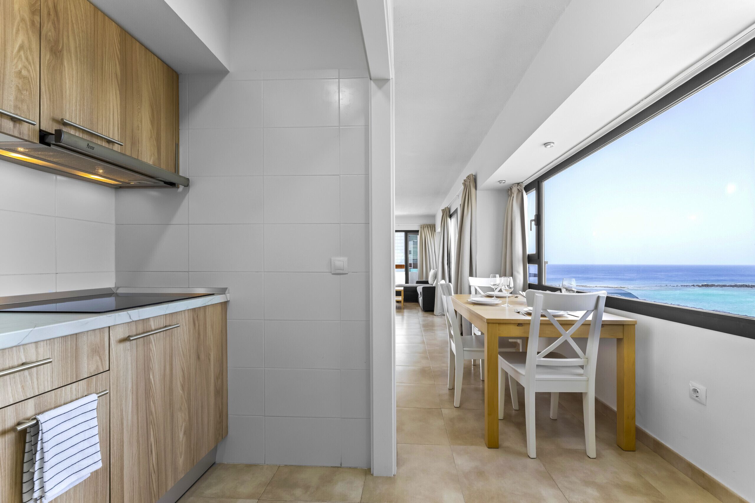 A modern kitchen with wooden cabinets, a stainless steel range hood, and a dining area with a table and chairs.