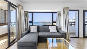 Ein modernes Wohnzimmer mit grauem Sofa, einem Glastisch und Meerblick durch große Fenster.