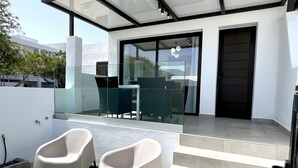 Une terrasse extérieure moderne, dotée d’une véranda en verre, d’un escalier menant à une porte et de deux chaises blanches.