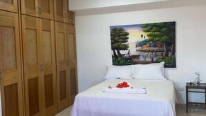A bedroom with a bed, a painting of a landscape, and wooden wardrobe doors. - Heavenly View (Cofresi)