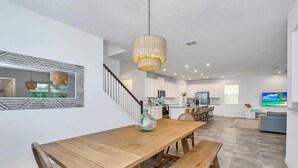 A spacious kitchen with white cabinets, a wooden dining table, and a hanging light fixture. - Solara Savings 2025 9BR Home w/private pool & games for 18 - Clubhouse Included (Four Corners)