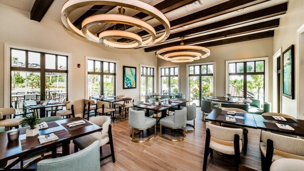 A modern dining area with multiple tables and chairs, large windows with natural light, and a unique circular ceiling light fixture. - Solara Savings 2025 9BR Home w/private pool & games for 18 - Clubhouse Included (Four Corners)