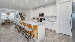 A modern kitchen with white cabinets, a large island with bar stools, a microwave, and a refrigerator. - Solara Savings 2025 9BR Home w/private pool & games for 18 - Clubhouse Included (Four Corners)