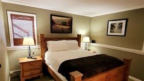 A neatly arranged bedroom with a wooden bed, two bedside tables with lamps, a window with blinds, and two framed pictures on the walls. - Ski, RIde, Walk On/Off Condo On Pico at Killington
 (Killington)