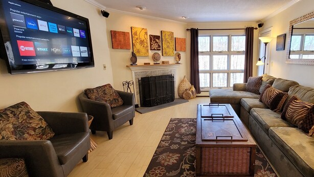 A living room with a fireplace, two sofas, a coffee table, and a flat-screen TV displaying entertainment apps. - Ski, RIde, Walk On/Off Condo On Pico at Killington
 (Killington)