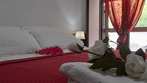 A bed with white linens, a red bedspread, and a bouquet of flowers on the side. - Rifugio Montano (Orsomarso)