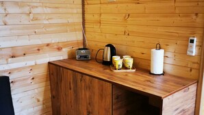 Interior de uma cabana de madeira com armário de madeira, um frigorífico pequeno, chaleira, rádio e tomada na parede.