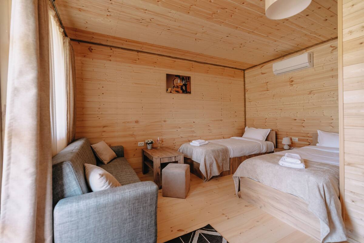 Une chambre de style cabane en bois, avec deux lits, un canapé, une petite table et un climatiseur fixé au mur.