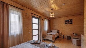 Quarto rústico estilo cabana, com duas camas, uma escrivaninha e um candeeiro pendente.