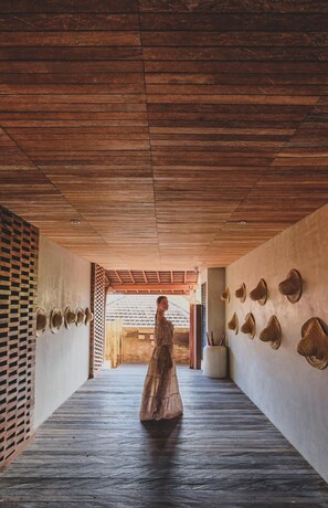 Un couloir avec un plafond en bois, une personne en robe et des chapeaux accrochés au mur.