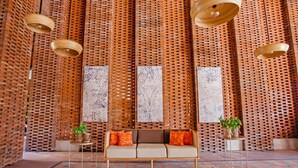 A room with a woven wooden partition, a sofa with orange cushions, and hanging wooden light fixtures. - Amnaya Resort Nusa Dua (Nusa Dua)