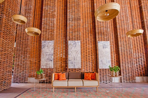 A room with a woven wooden partition, a sofa with orange cushions, and hanging wooden light fixtures. - Amnaya Resort Nusa Dua (Nusa Dua)