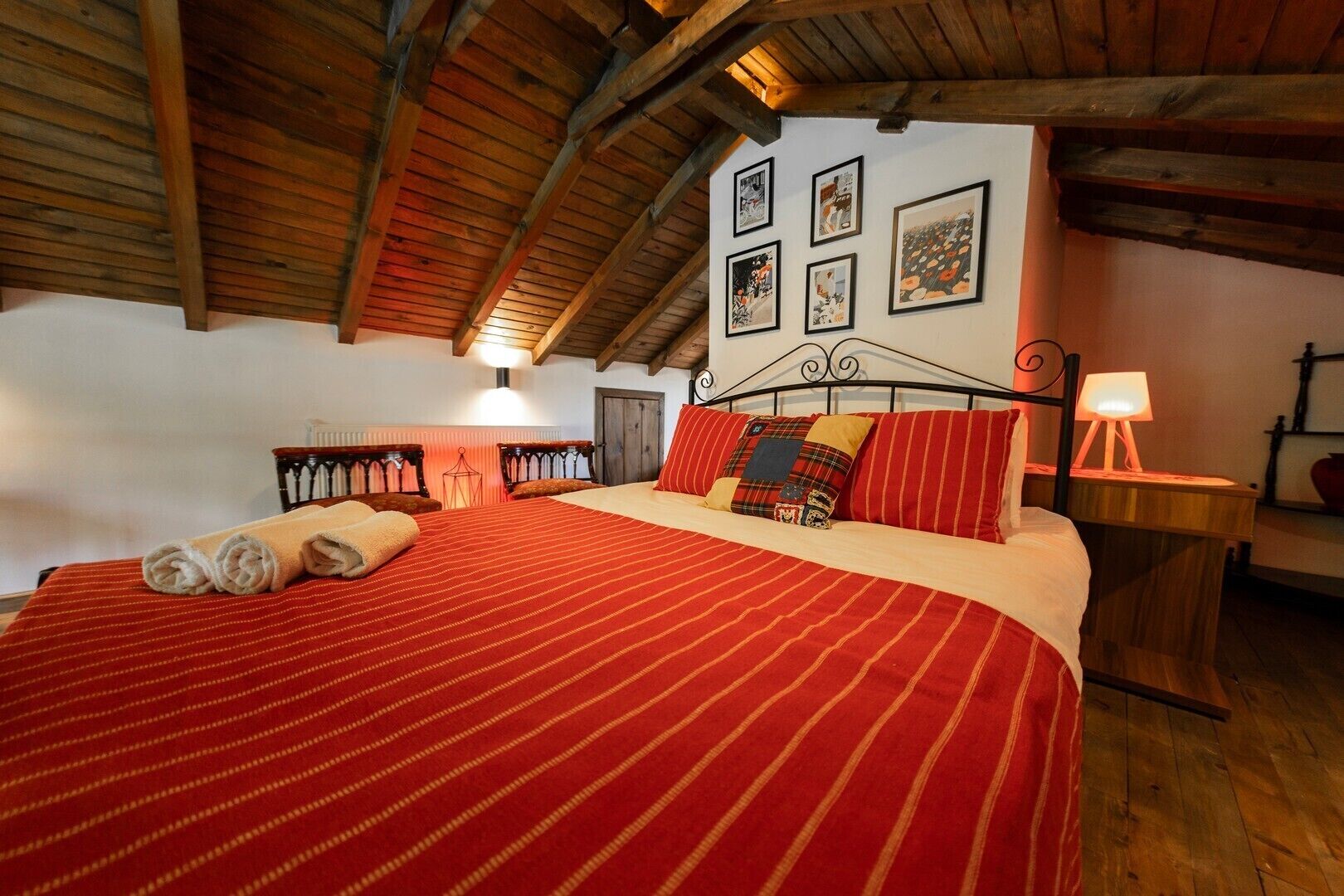 A cozy bedroom with a large bed, wooden beams, and framed pictures on the wall.