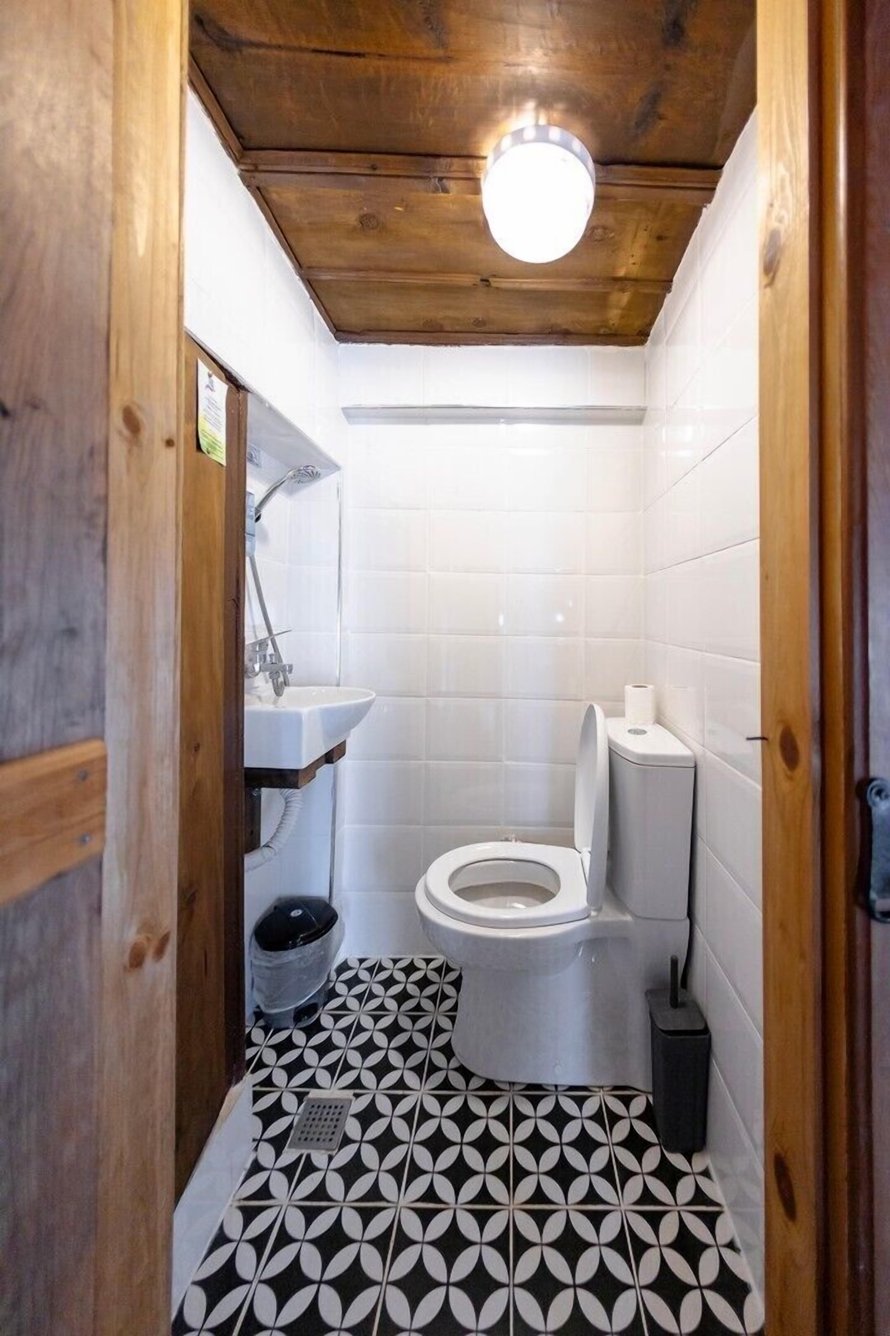 A small, compact bathroom with a toilet, sink, and shower. The floor has a geometric tile pattern.
