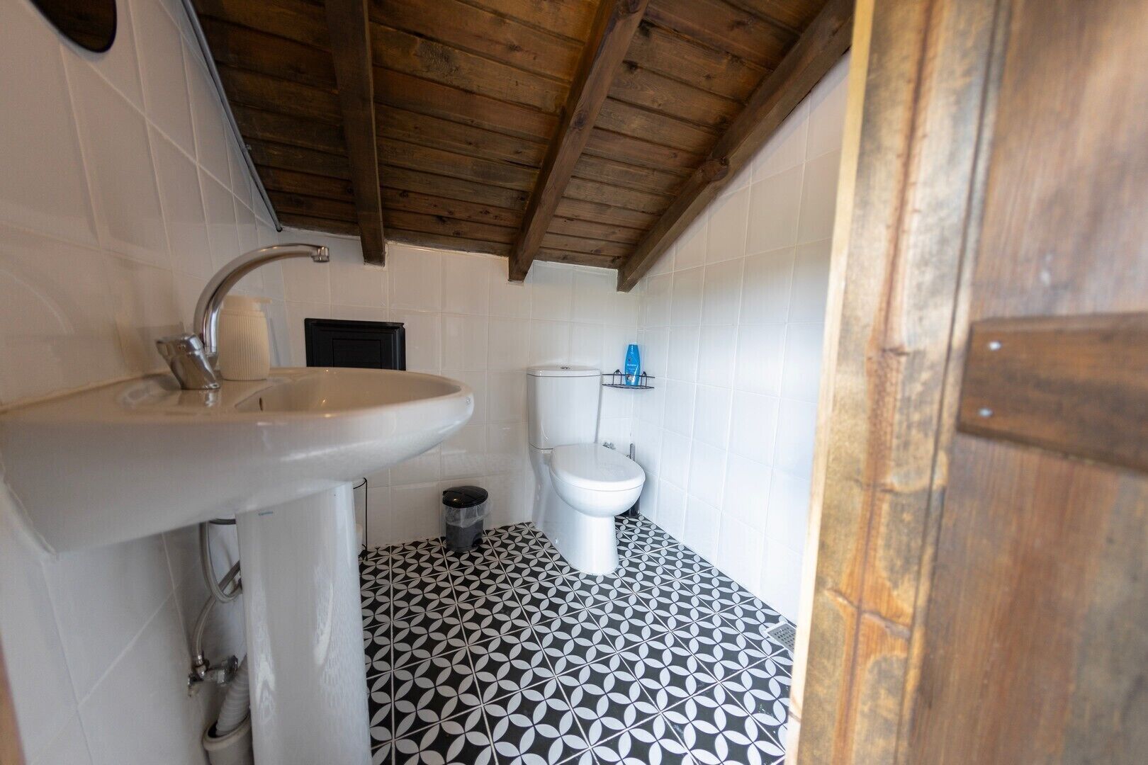 A small bathroom with a sink, toilet, and patterned floor tiles.