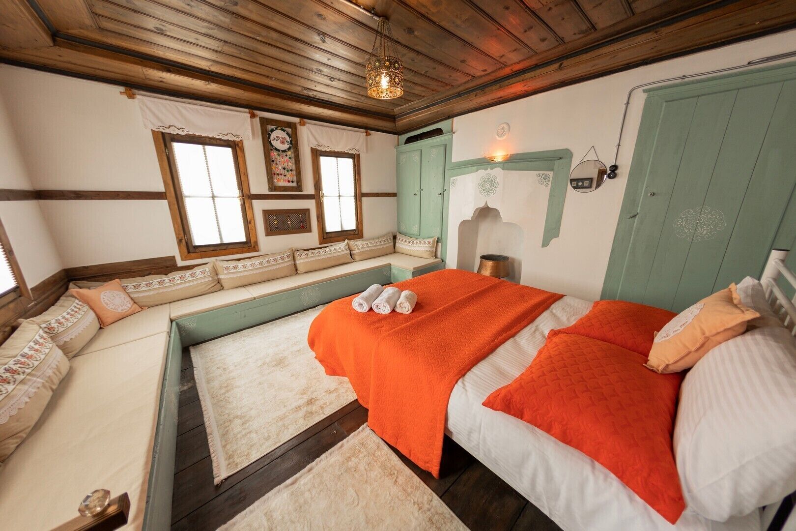 A cozy room with a large bed, a bench with cushions, a wall-mounted light, and a wooden ceiling.