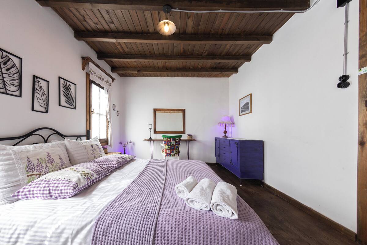 A bedroom with a bed, a wooden ceiling, a dresser, and wall decorations.
