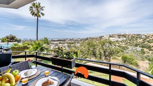 Un balcon avec une table dressée pour le petit-déjeuner, offrant une vue panoramique sur un paysage magnifique, avec la ville et les collines en toile de fond.