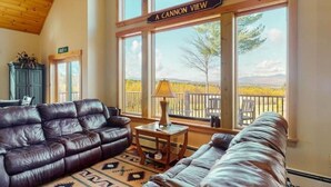 A cozy living room with a leather couch, a side table with a lamp, and a view of a fenced area with trees.