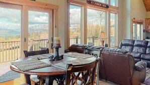 A spacious living area with a large window offering a view of the mountains, a dining table with placemats, and a leather sofa.