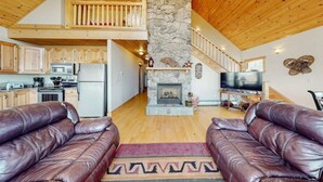 A spacious living area with a stone fireplace, wooden ceiling, and a television.