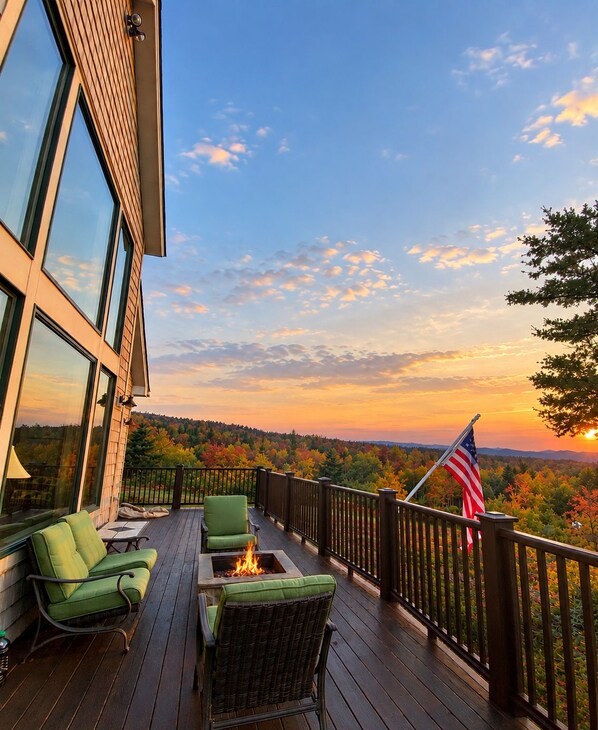 A deck with outdoor furniture and a fire pit, overlooking a forested landscape.