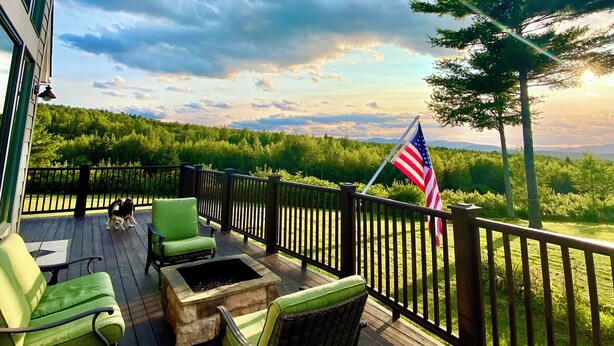 A wooden deck with outdoor furniture, a flag, and a view of a forested landscape.