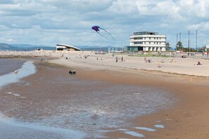Een strand met een modern gebouw, een vlieger en mensen die ontspannen.
