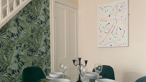 A dining area with a glass table, four green chairs, white plates, and wine glasses. A white door and a staircase are visible in the background. - Spacious Lancaster city centre hide away with garden. (Lancaster)