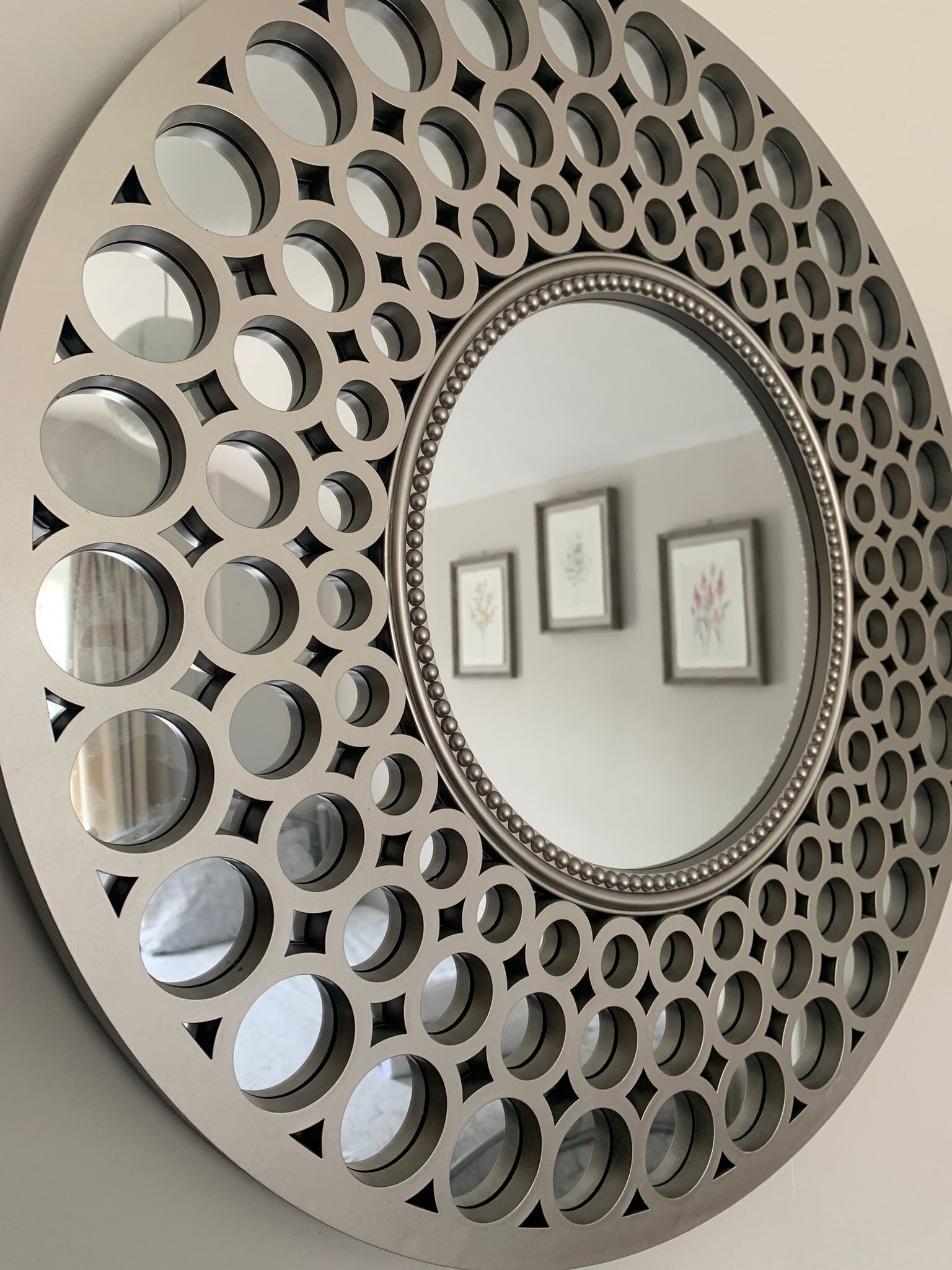 Decoración de pared circular con un espejo central rodeado por un marco metálico decorativo con diseños circulares.