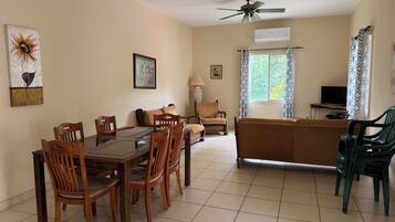 A living room with a dining table, chairs, a sofa, a TV, and a ceiling fan.