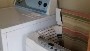 Ein Waschbereich mit Waschmaschine und Trockner, einem gestreiften Handtuch und einem Kleiderständer mit einem bunten Gegenstand.