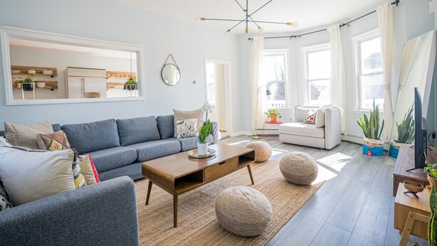 A modern living room with a grey sofa, wooden coffee table, and a dining area with a wooden table and chairs.